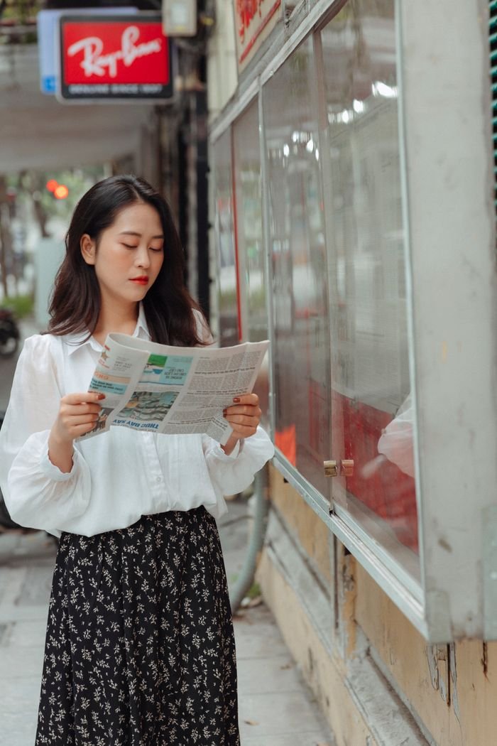 Crafting Captivating Headlines: Your awesome post title goes here Fashionable woman in white blouse reads newspaper while standing on city street.