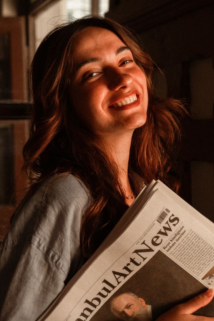 The Art of Drawing Readers In: Your attractive post title goes here A smiling young woman holding an art newspaper while standing indoors.