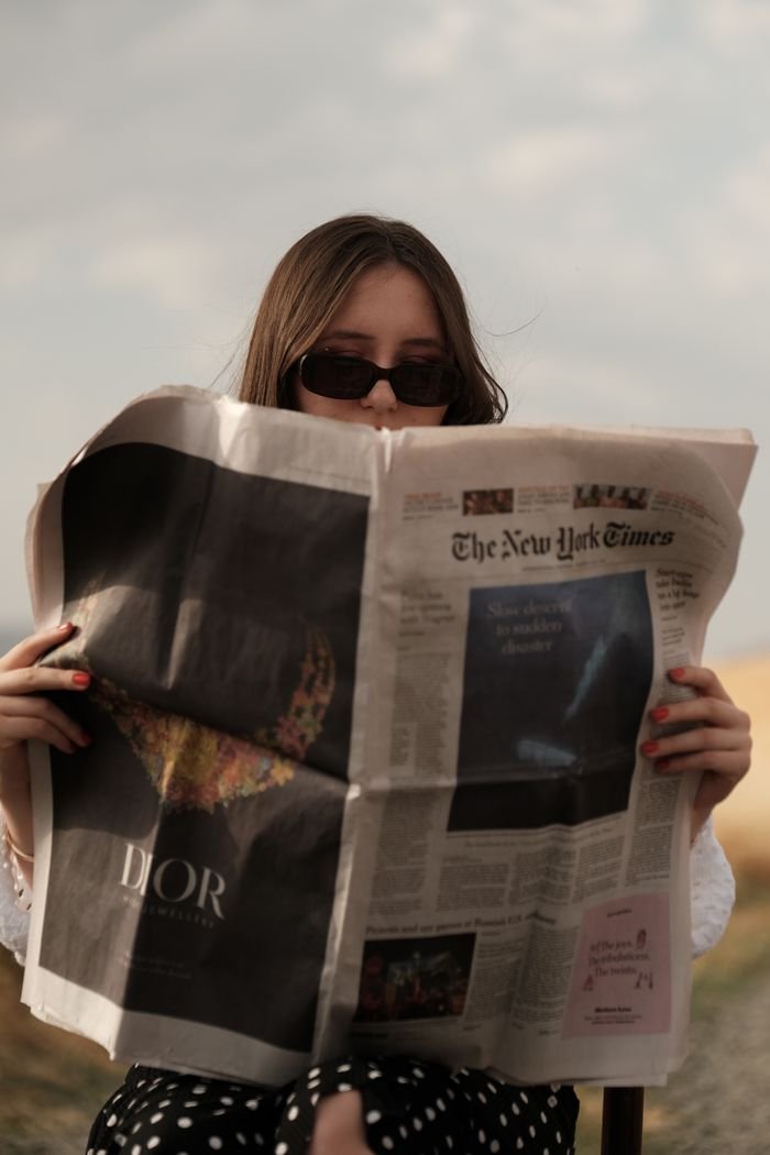Home An adult woman enjoys reading The New York Times while sitting outdoors on a sunny day.