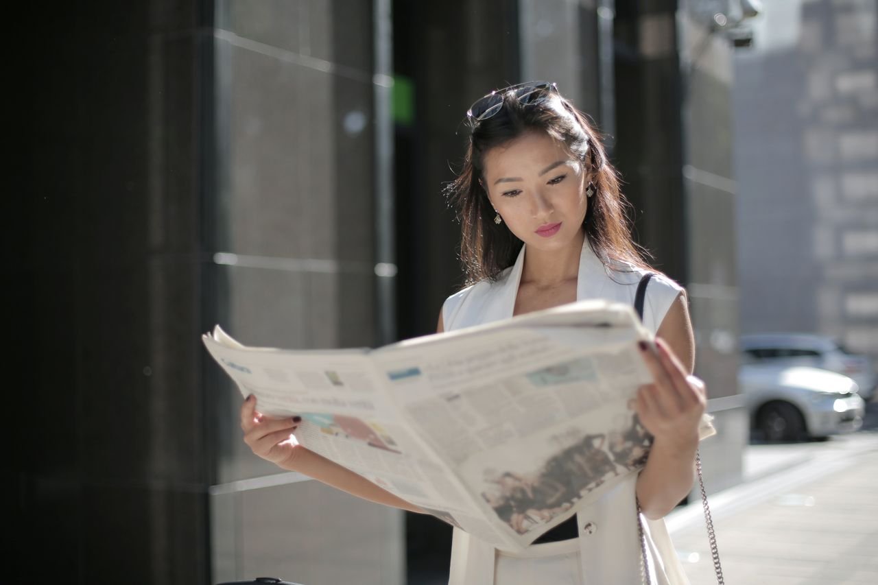 About Stylish woman reading a newspaper on a sunny day in the city.